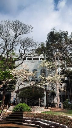 a large white building with lots of trees in the front yard and stairs leading up to it