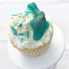 a cupcake with white frosting and blue sprinkles on a plate