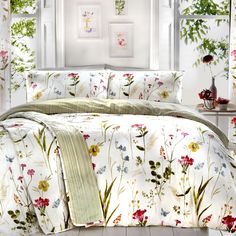 a bed covered in a white comforter next to a wall with flowers on it