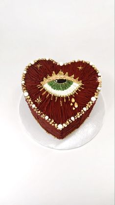 a heart shaped cake on a plate with beads and pearls around the edges, decorated with an eye