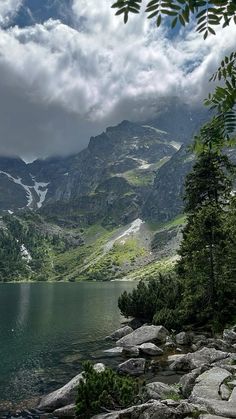 a mountain lake surrounded by rocks and trees with clouds in the sky above it, on a cloudy day