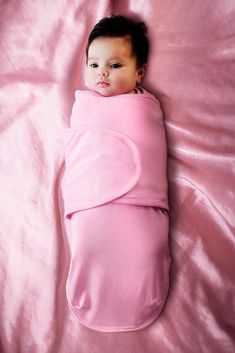 a baby wrapped in a pink blanket laying on top of a pink bedding sheet