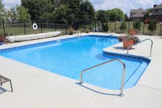 an empty swimming pool with chairs around it and fenced in area behind the pool