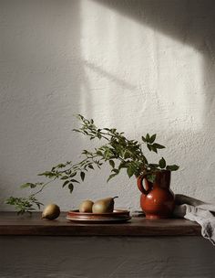 an orange vase and some pears on a wooden table next to a white wall