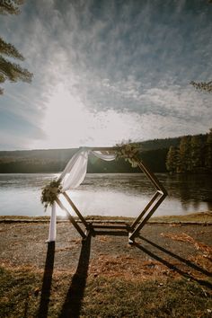 an outdoor ceremony setup with white draping and greenery on the grass near a body of water