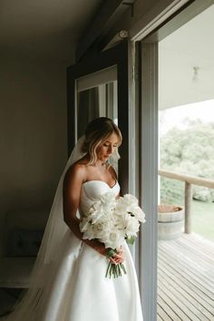 a woman in a wedding dress standing on a porch holding a bouquet of white flowers