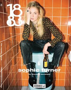 a woman sitting on top of a blue stool next to a tiled wall and holding a bottle