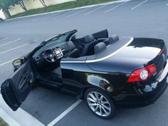 a black convertible car parked in a parking lot with its doors open and the top down