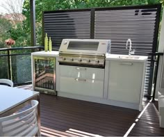 an outdoor kitchen with grill, sink and table on the deck overlooking the backyard area