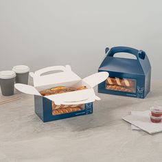 two blue boxes with pastries in them sitting on a table next to coffee cups