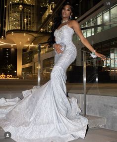 a beautiful woman in a white dress standing on some steps outside at night with her hand on the railing