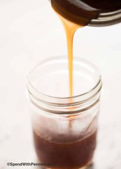 caramel sauce being poured into a mason jar filled with chocolate cake mix on a white surface