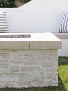 a stone bench sitting on top of a green grass covered field next to a white wall