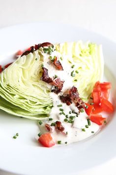 a white plate topped with lettuce covered in ranch dressing and sliced tomato wedges