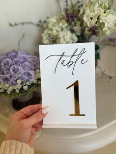 a person holding up a table number with flowers in the background