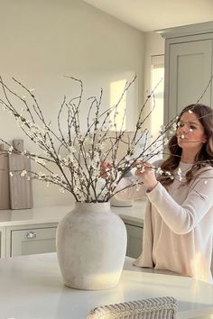 a woman arranging flowers in a white vase