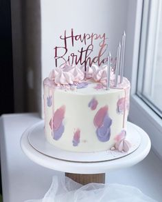 a white cake with pink and purple frosting on it sitting on top of a table next to a window