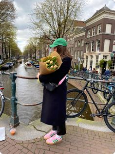 a woman standing on the edge of a bridge holding flowers in her hand and looking at the water