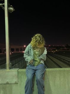 a woman leaning against a wall with her hand on her hip looking at her cell phone