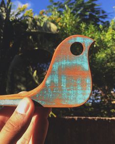 a hand holding an orange and blue bird shaped object in front of some trees on a sunny day