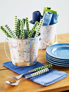 a wooden table topped with plates and cups filled with green napkins next to a map bucket