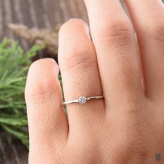 a woman's hand with a diamond ring on top of her finger, next to some greenery