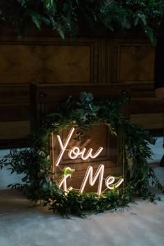 a sign that says you and me is lit up in front of some greenery