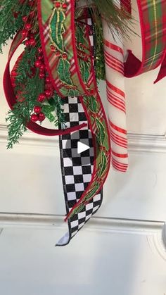 a christmas wreath hanging on the front door with red, green and white ribbons attached to it