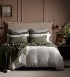 a bed with green and white linens in a pink room next to a wooden table