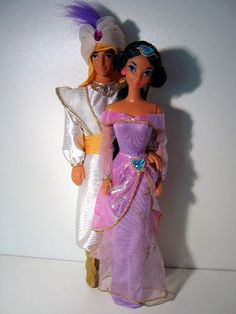 two dolls are dressed in purple and white outfits, one is holding the other's hand