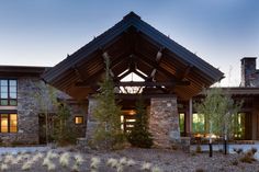 a large stone building with a wooden roof and tall trees in front of it at dusk