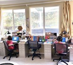 two children are sitting at desks in front of large windows with books on them