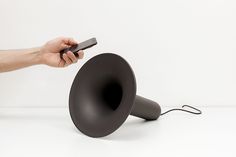 a hand holding a remote control next to a black bullhorn shaped object on a white surface