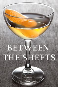 the cover of between the sheets, with an orange slice in a martini glass on a wooden table