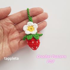 a crocheted strawberry with a flower on it's end sitting in someones hand