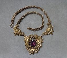 "Opulent and touch flamboyant, pendant front necklace in a Rococo style, crafted in an antiqued gold tone metal. Central, wide oval part has three swirling, deeply indented and nicely detailed Acanthus leaves in curving, asymmetrical lines. Leaves are sheltering \"floating\" and multiprong set in a low bezel frame, faceted, amethyst colored glass. Glass is foiled, in an open backed setting. Small Etruscan knob is placed above glass stone and open space is left on the sides. Two curled upward lea Rococo Revival, Hand Jewelry Rings, Acanthus Leaves, Fancy Necklace, Magical Jewelry, Amethyst Color, Rococo Style, Funky Jewelry, Jewelry Lookbook