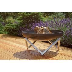 a fire pit sitting on top of a wooden deck next to purple flowers and trees