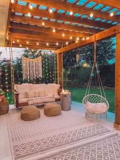 an outdoor living area with hanging chairs, couches and lights on the ceiling is lit up by string lights