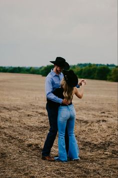 a man and woman standing in the middle of an open field with their arms around each other