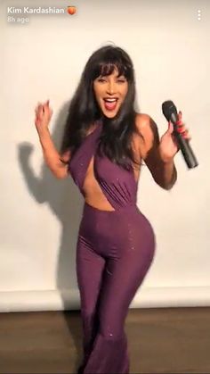 a woman in a purple jumpsuit holding a microphone and singing into a karaoke