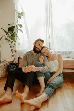 a man and woman sitting on the floor in front of a window with their arms around each other