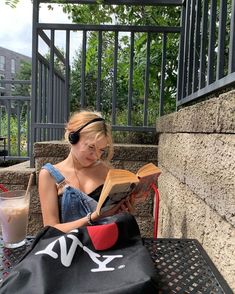 a woman reading a book while sitting at an outdoor table with a glass of milk