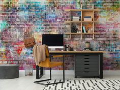 a desk with a computer on it in front of a colorful brick wall that has been painted