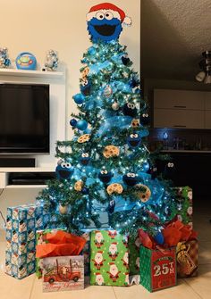 a blue christmas tree with presents under it and a cookie monster decoration on the top