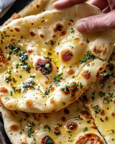 a hand is picking up a piece of flat bread with cheese and herbs on it