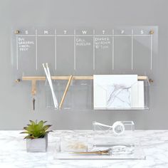 a clear acrylic calendar hanging on a wall next to a potted plant