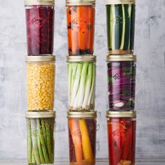 six jars filled with different types of vegetables and beans, all lined up on top of each other