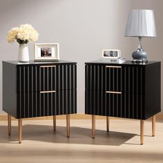 two black and gold nightstands with pictures on them next to a white flower vase