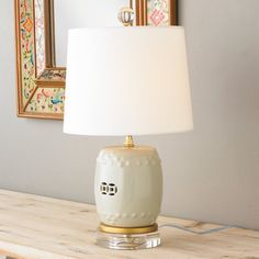 a white lamp sitting on top of a wooden table next to a framed picture and mirror