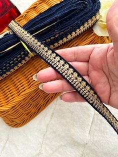 a hand holding a pair of blue and gold hair clips in front of a wicker basket